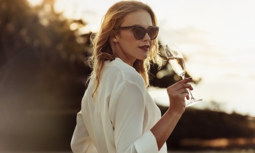 a woman sipping on wine outdoors in a bright dress