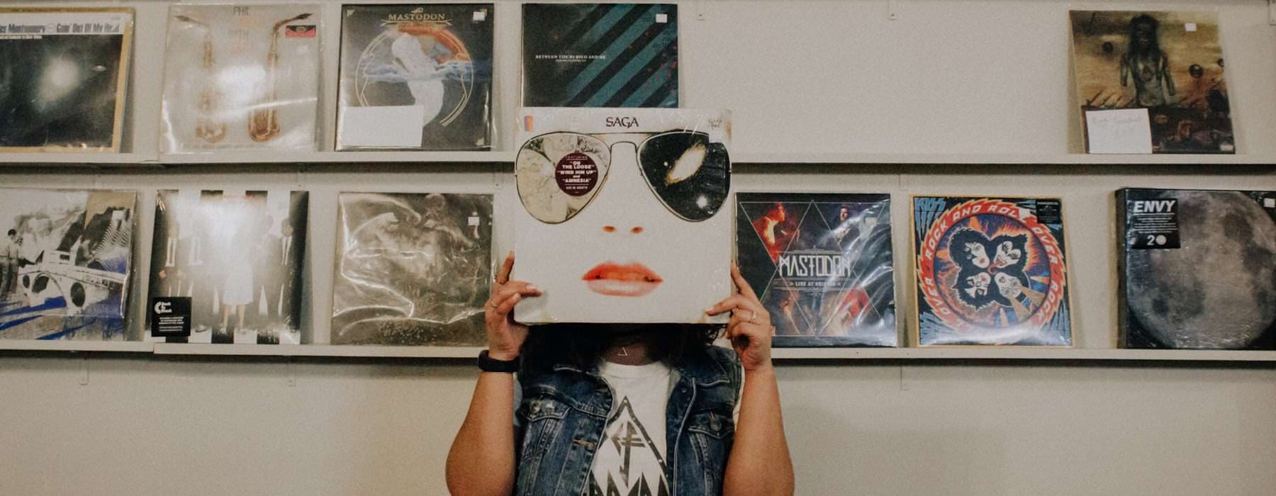 resident holds vinyl cover in front of their face in front of a wall with more covers on shelves